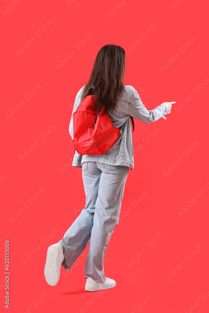 Female student with backpack pointing at something on red background, back view