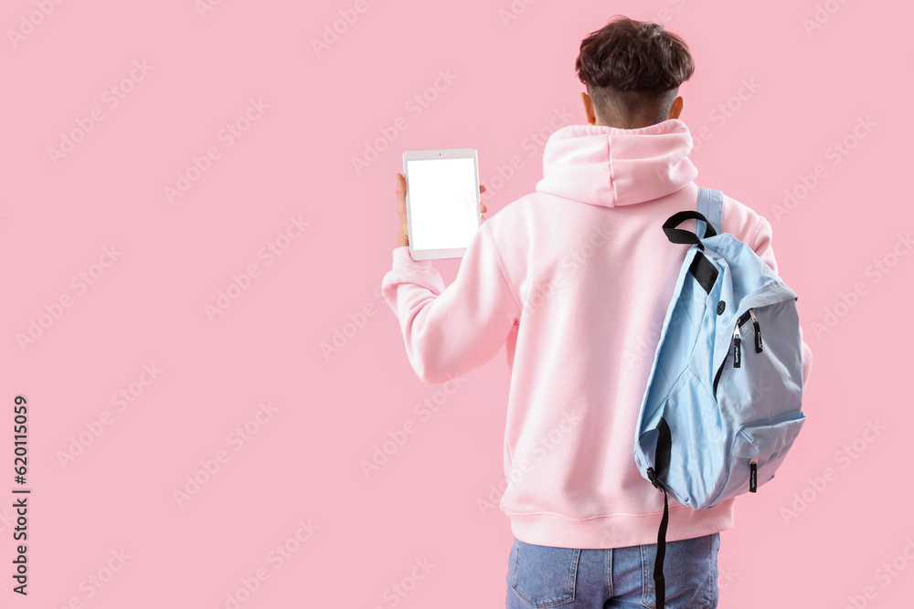 Male student with tablet computer and backpack on pink background, back view