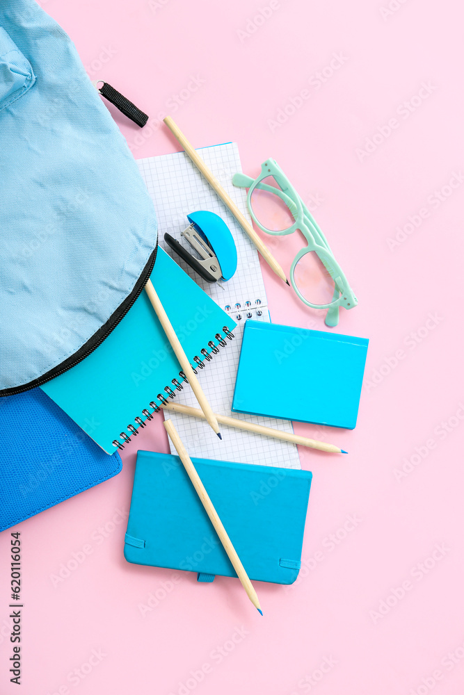 Blue school backpack with notebooks, color pencils and eyeglasses on pink background