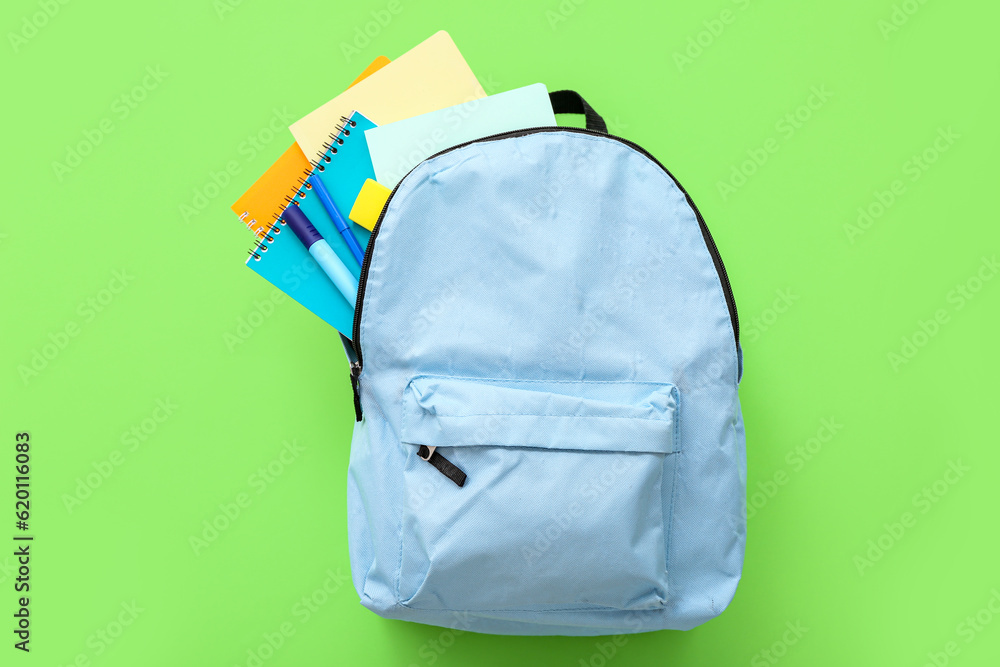 Blue school backpack with notebooks and markers on green background