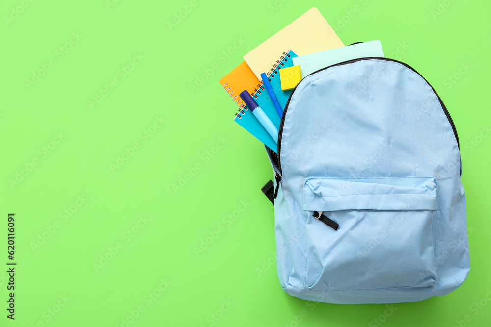 Blue school backpack with notebooks and markers on green background