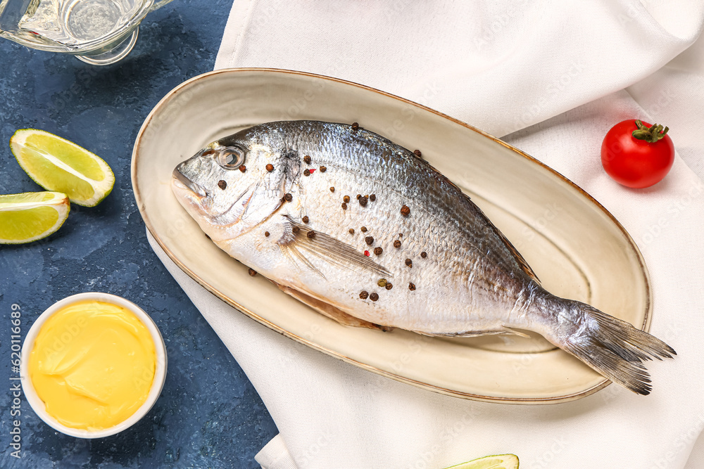 Plate of raw dorado fish with lime and sauce on blue background