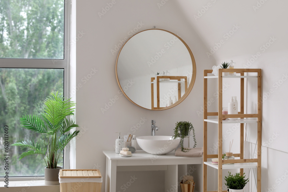 Interior of light bathroom with sink bowl, bath accessories, mirror and shelving unit