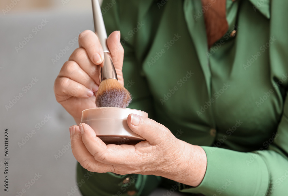 Senior woman with makeup brush and powder at home, closeup