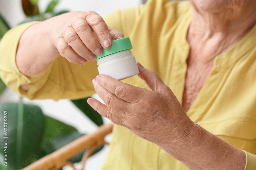 Senior woman with jar of cream at home, closeup