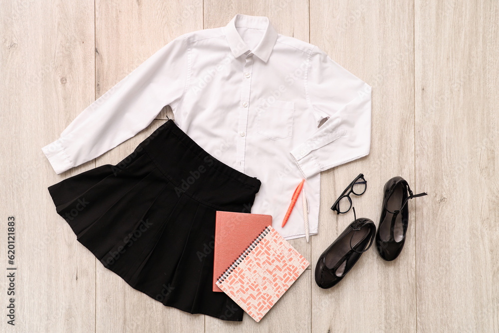 Composition with stylish school uniform, shoes, eyeglasses and stationery on wooden background