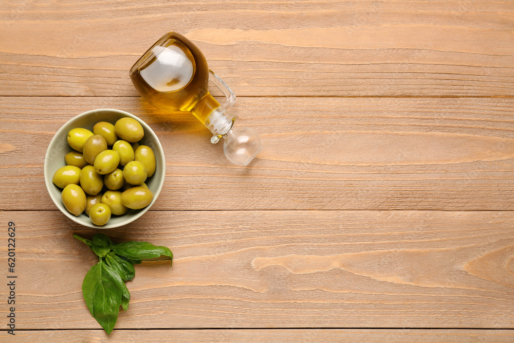 Bowl with ripe olives and jug of oil on wooden background