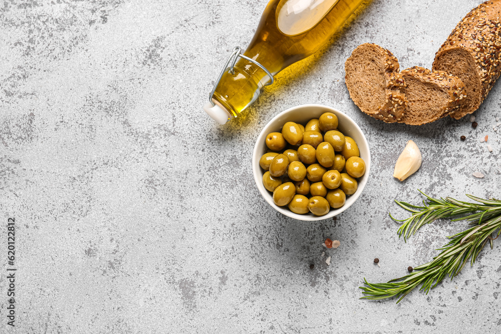 Bowl with ripe olives, bread and bottle of oil on light background