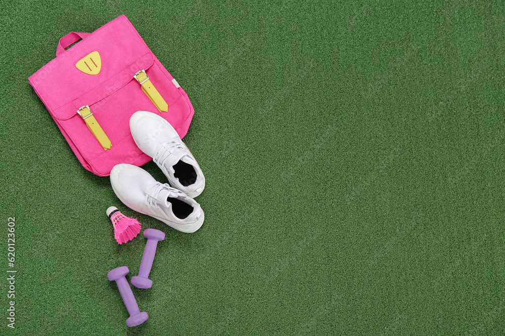 Backpack with sneakers, badminton shuttlecock and dumbbells on color background