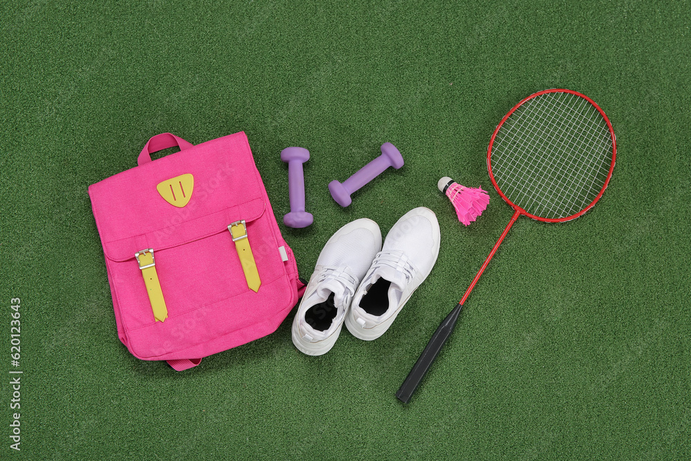 Backpack with sneakers, badminton shuttlecock and dumbbells on color background