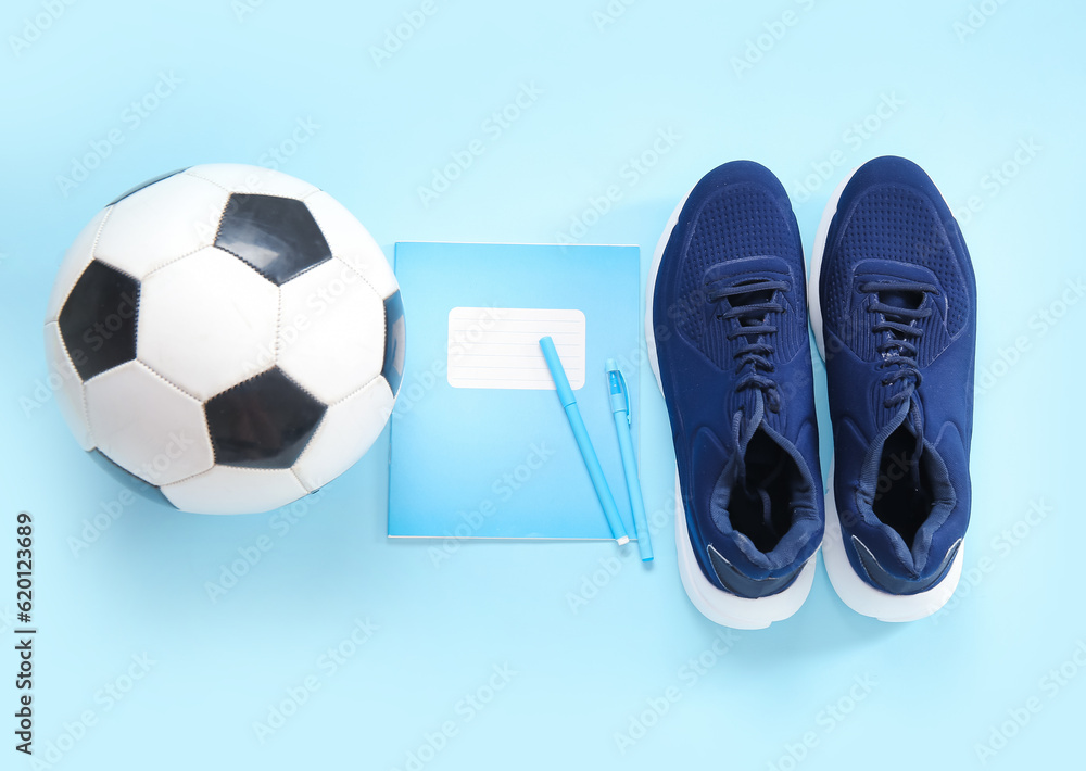 Sneakers with soccer ball, notebook and pens on blue background