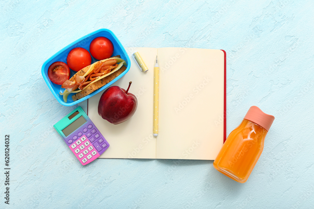 Stationery, drink and lunch box with tasty food on blue background