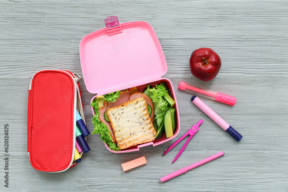 Stationery and lunch box with tasty food on grey wooden background