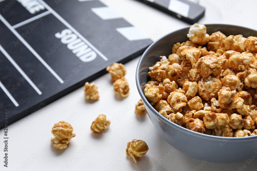 Bowl with tasty popcorn and clapperboard on white background