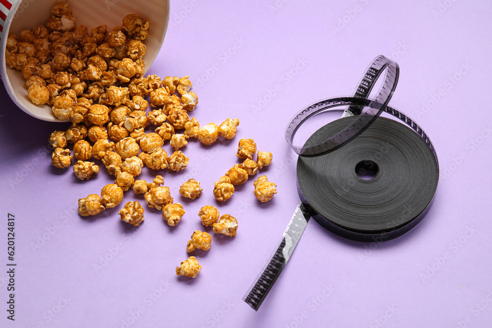 Bucket with tasty popcorn and film reel on purple background