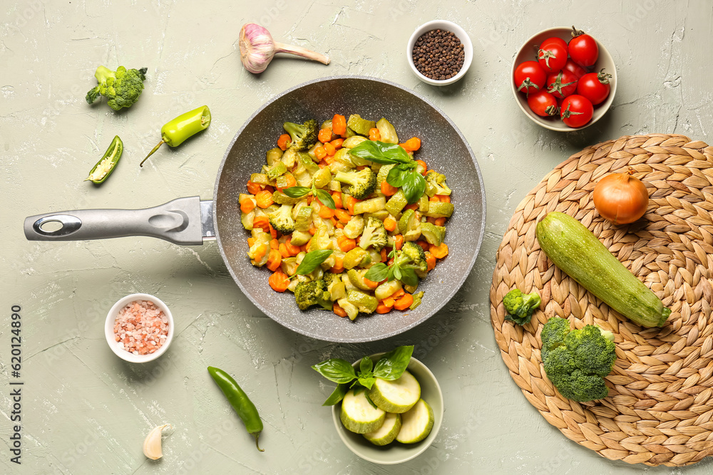 Frying pan with different vegetables on light background