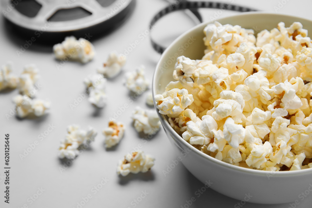 Bowl with tasty popcorn and film reel on grey background