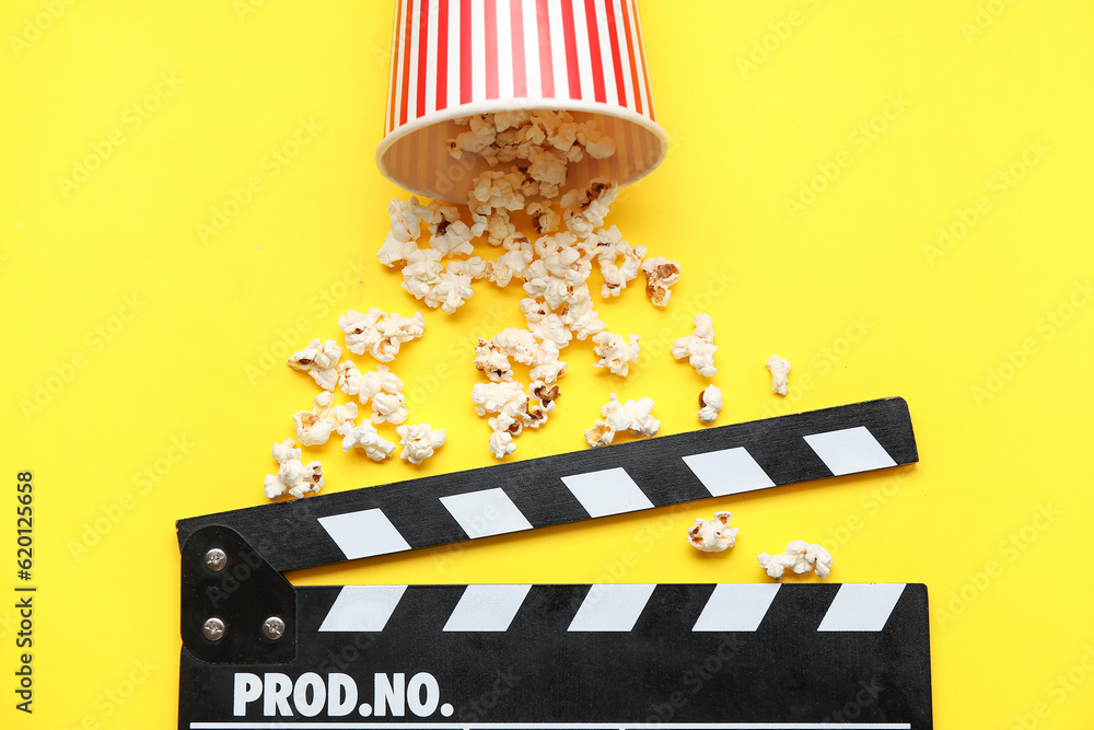 Bucket with tasty popcorn and clapperboard on yellow background