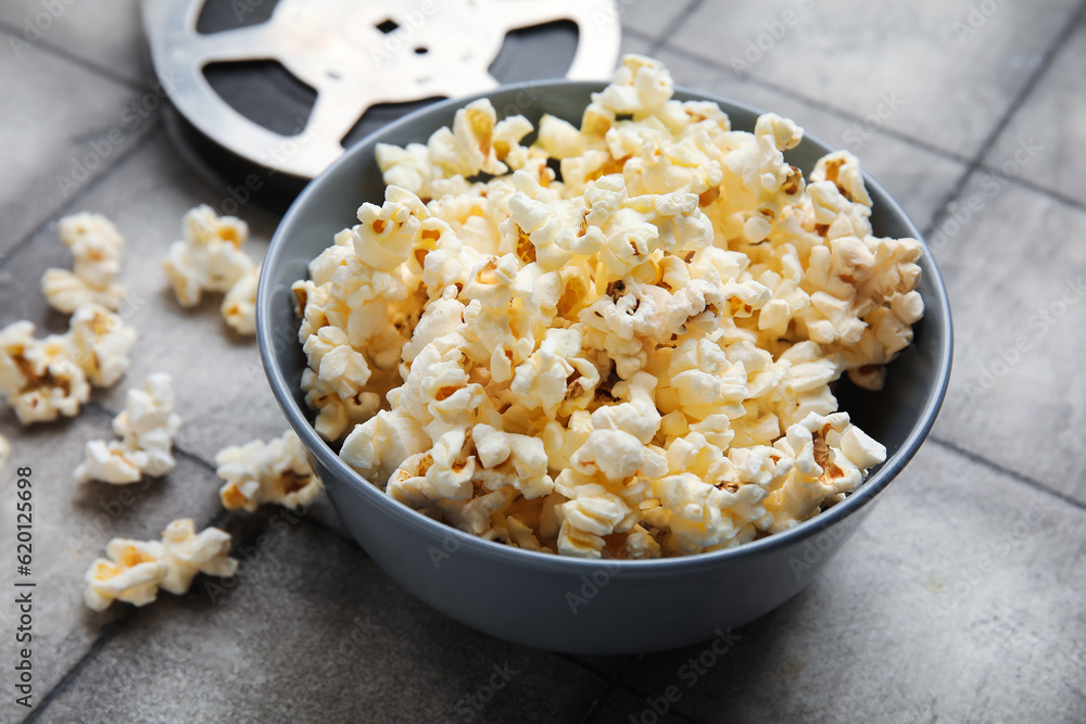 Bowl with tasty popcorn and film reel on grey tile background