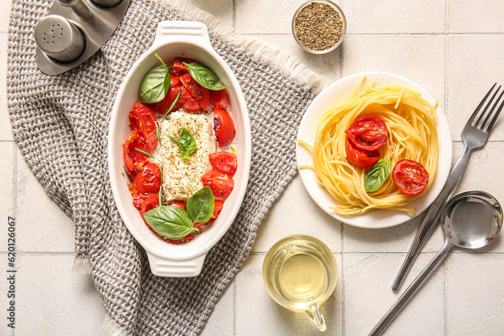 Baking dish with tasty tomatoes, feta cheese and pasta on white tile background