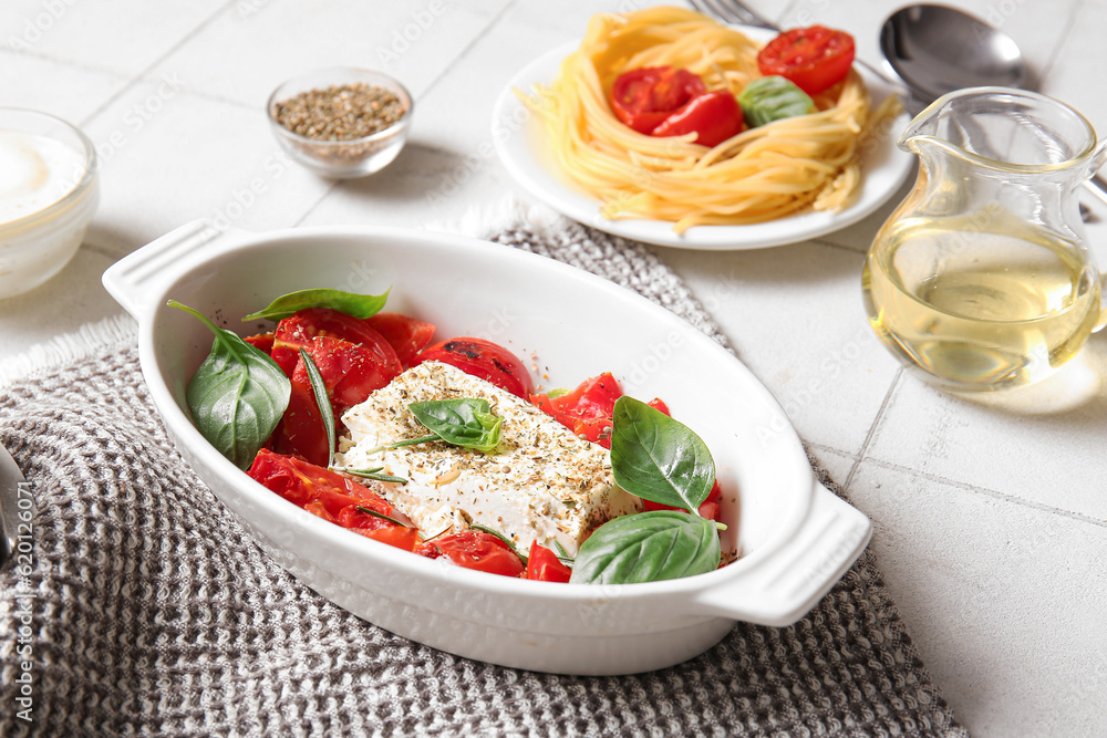 Baking dish with tasty tomatoes and feta cheese on white tile background