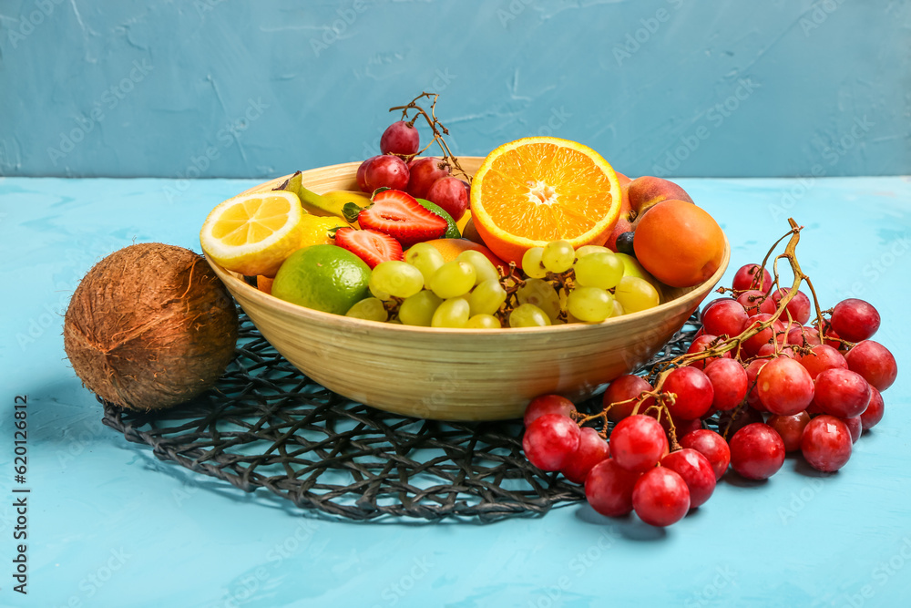 Bowl with different fresh fruits on blue background