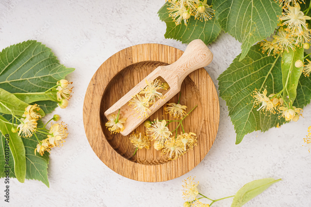 Composition with wooden plate, scoop, aromatic linden flowers and leaves on light background