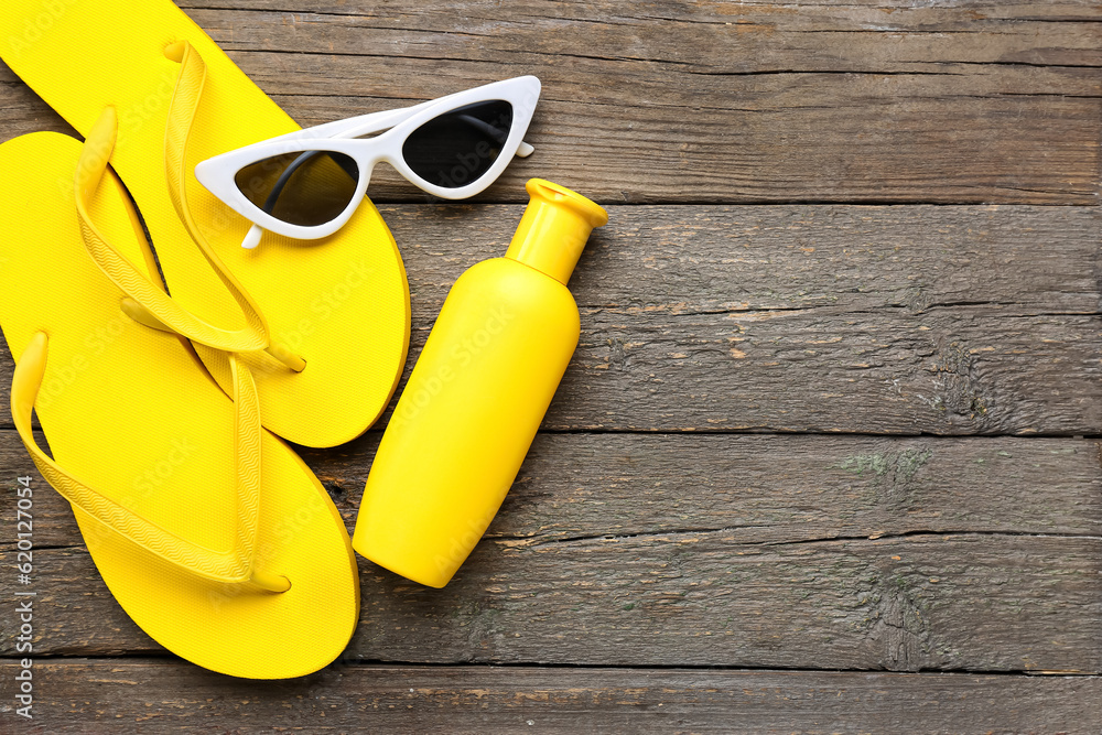 Sunglasses with flip flops and bottle of sunscreen cream on brown wooden background