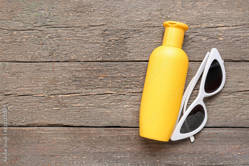 Sunglasses with bottle of sunscreen cream on brown wooden background