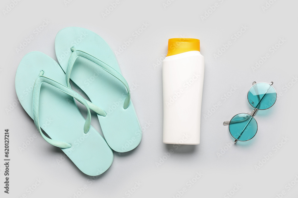 Sunglasses with flip flops and bottle of sunscreen cream on grey background