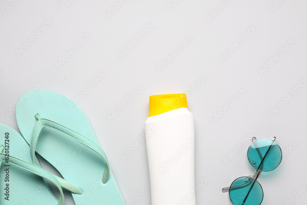 Sunglasses with flip flops and bottle of sunscreen cream on grey background