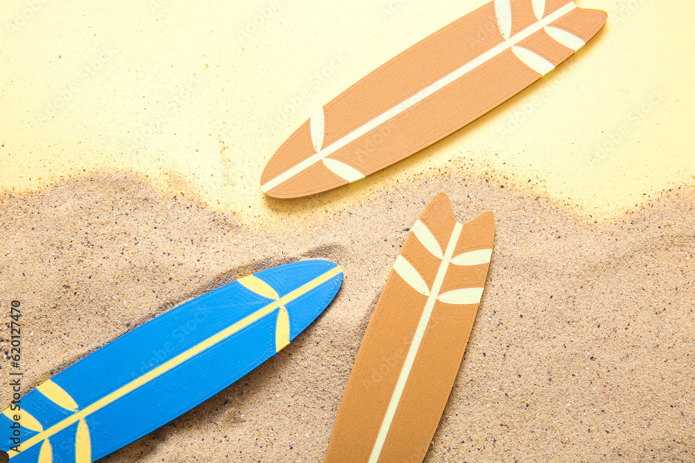 Mini colorful surfboards on sand against pale yellow background