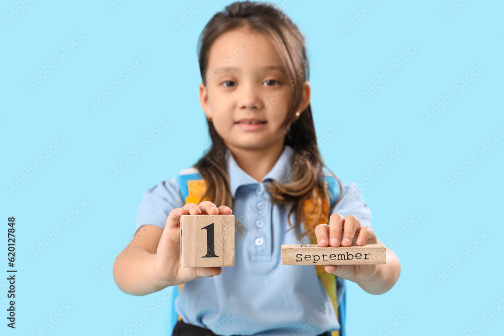 Little schoolgirl with calendar on light blue background