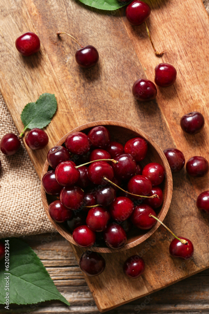 Wooden board with bowl of sweet cherries, closeup