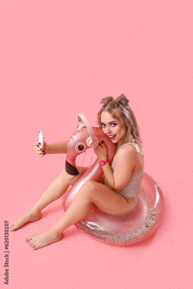 Young woman in swimsuit with mobile phone and inflatable ring on pink background