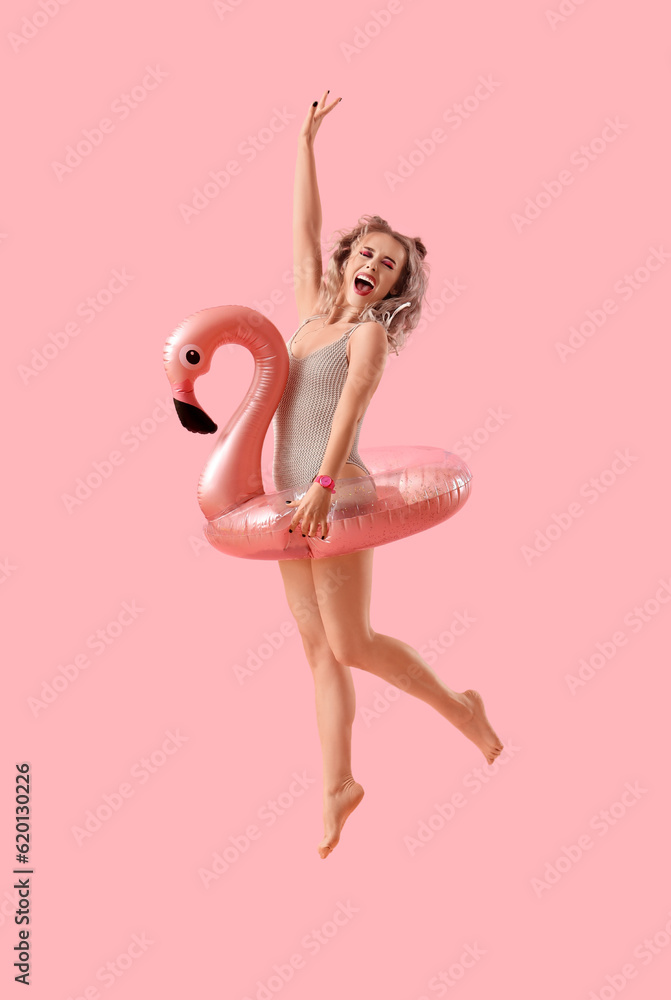 Young woman in swimsuit with inflatable ring jumping on pink background