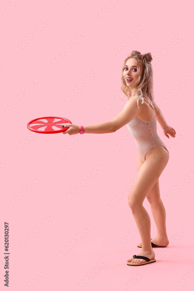 Young woman in swimsuit with frisbee disk on pink background