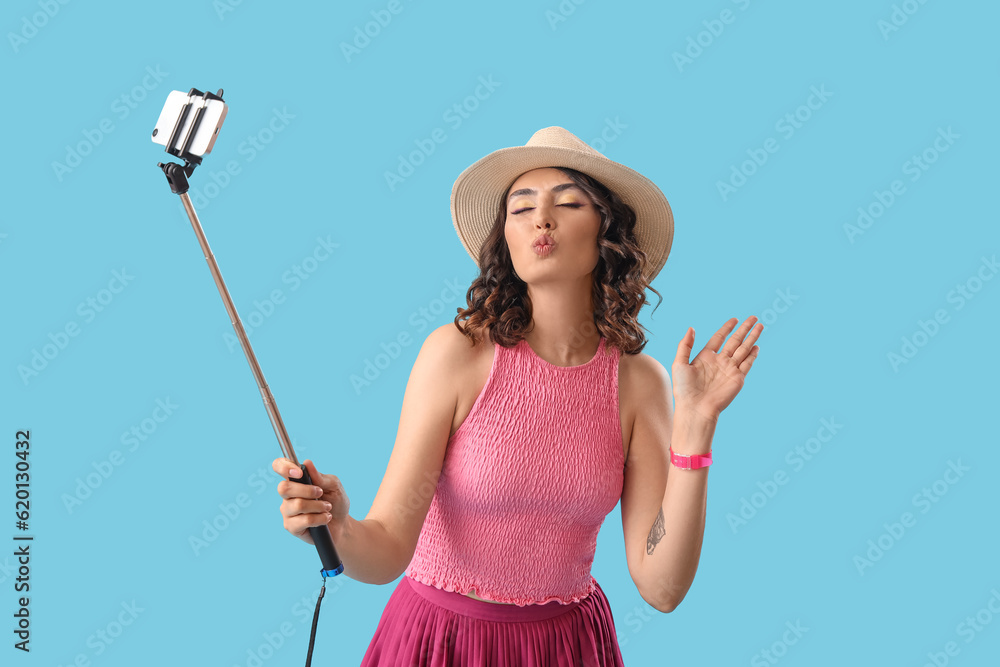 Young woman with mobile phone taking selfie on blue background