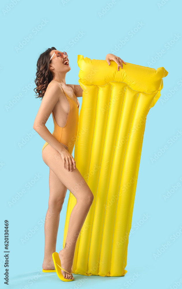 Young woman in swimsuit with inflatable mattress on blue background