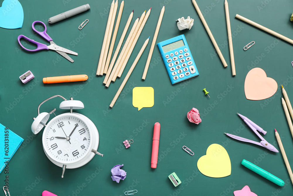 Alarm clock with different stationery on green chalkboard