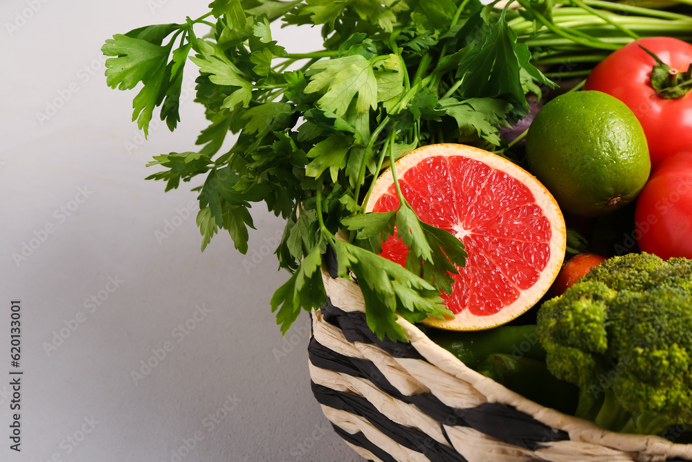 Wicker bowl with different fresh fruits and vegetables on white background, closeup