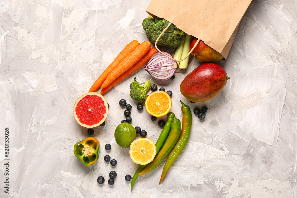 Paper bag with different fresh fruits and vegetables on grey background