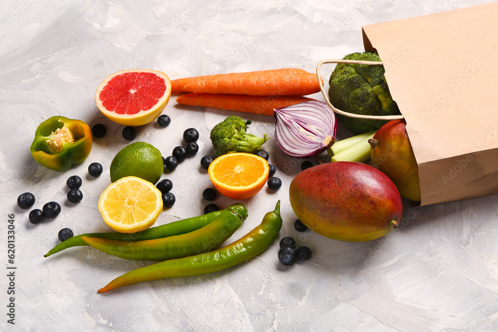 Paper bag with different fresh fruits and vegetables on grey background