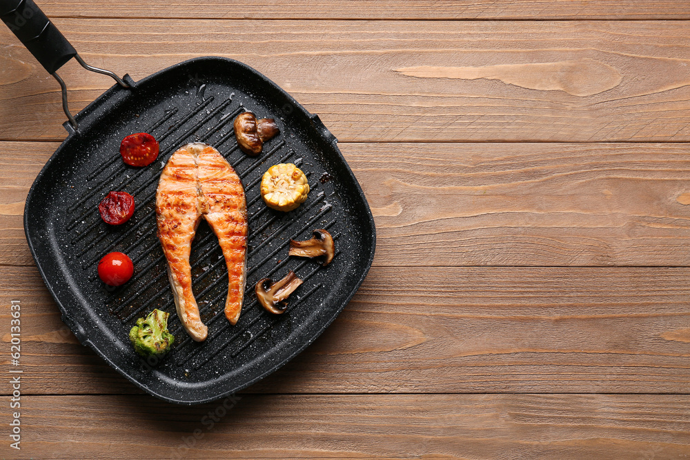 Frying pan with tasty grilled salmon steak and vegetables on wooden background