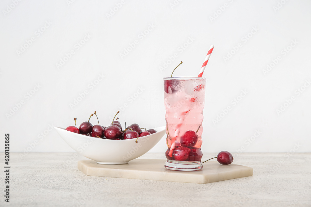 Glass of tasty cherry lemonade and bowl with berries on white background