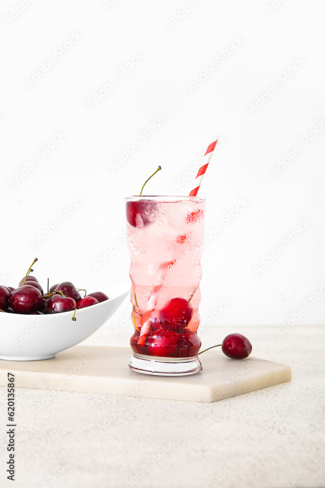 Glass of tasty cherry lemonade and bowl with berries on white background