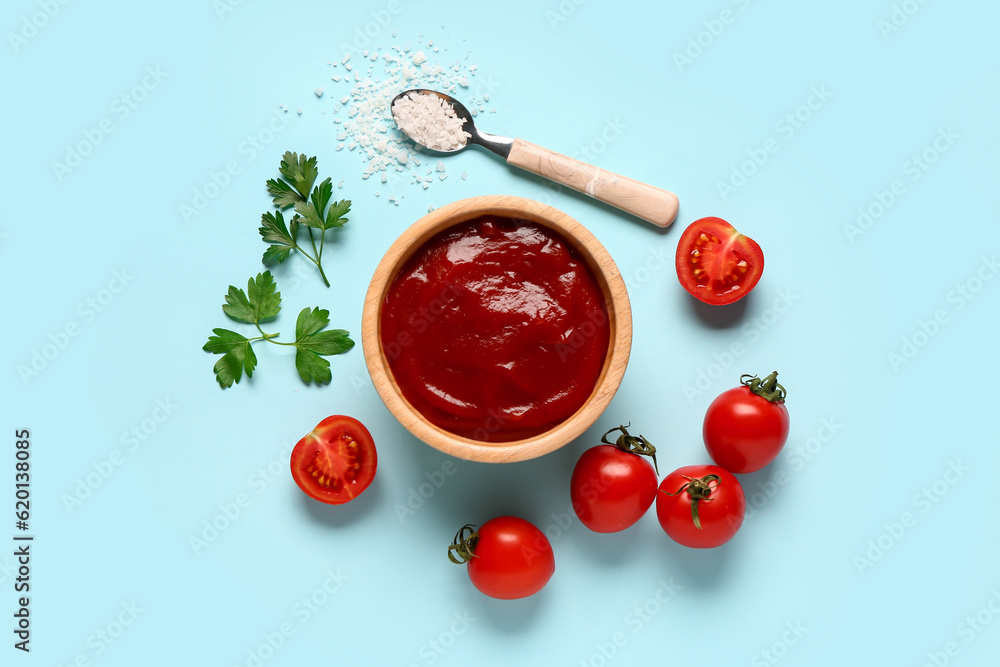 Bowl with tomato paste and fresh vegetables on blue background