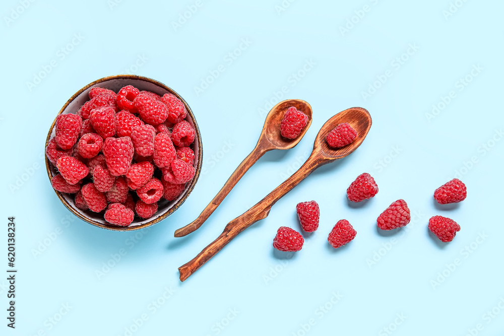 Bowl and spoons with fresh raspberries on blue background