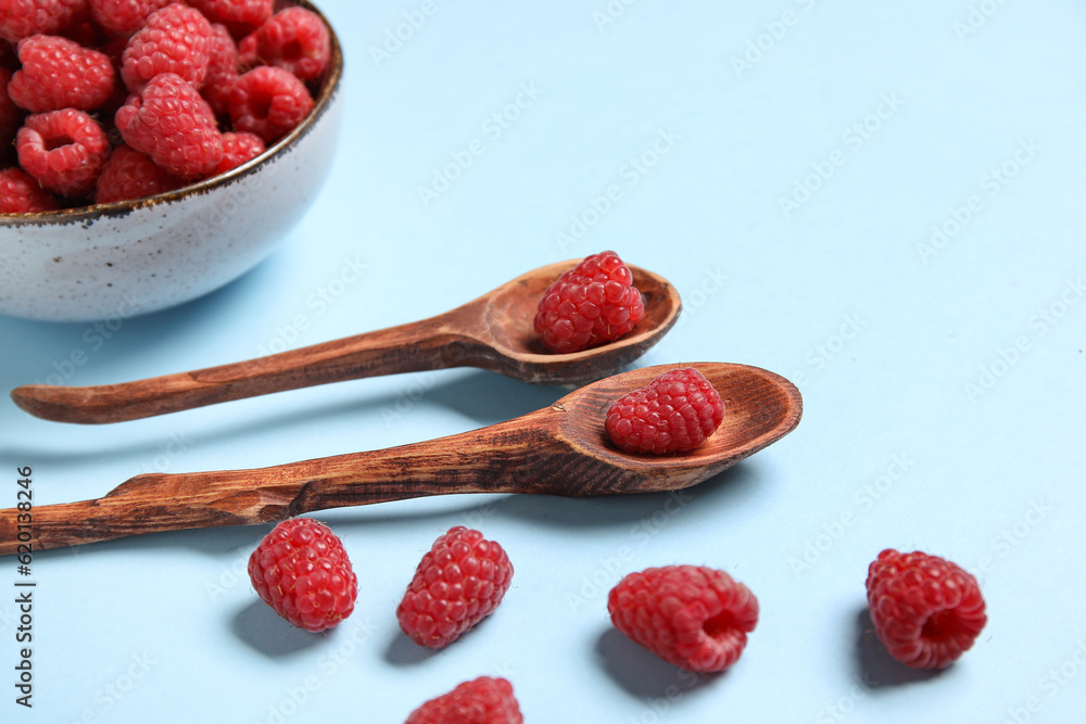 Bowl and spoons with fresh raspberries on blue background