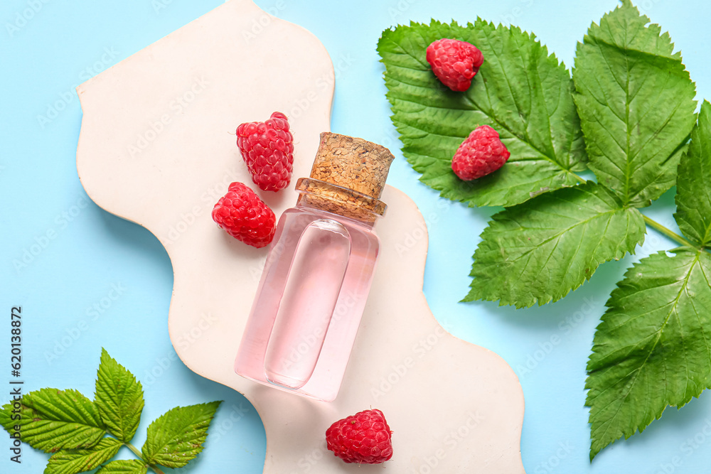 Decorative podium with bottle of cosmetic raspberry oil on blue background